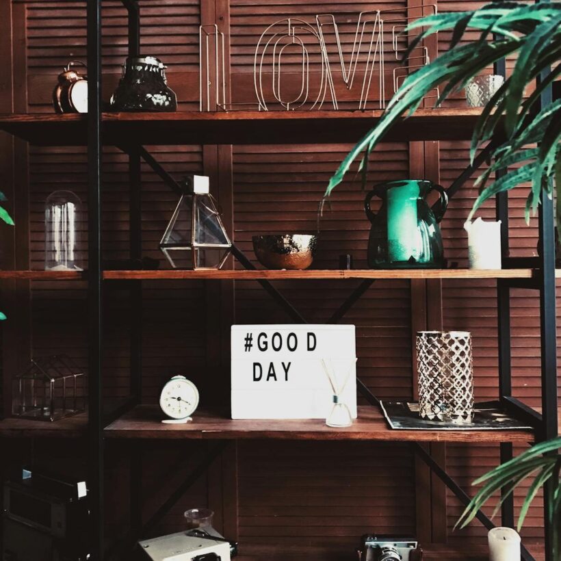 Modern interior shelf rack with assorted decorations and glowers and light box with tag Good day